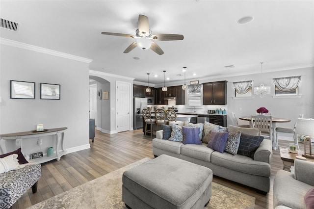 living room with ceiling fan with notable chandelier, wood-type flooring, sink, and crown molding