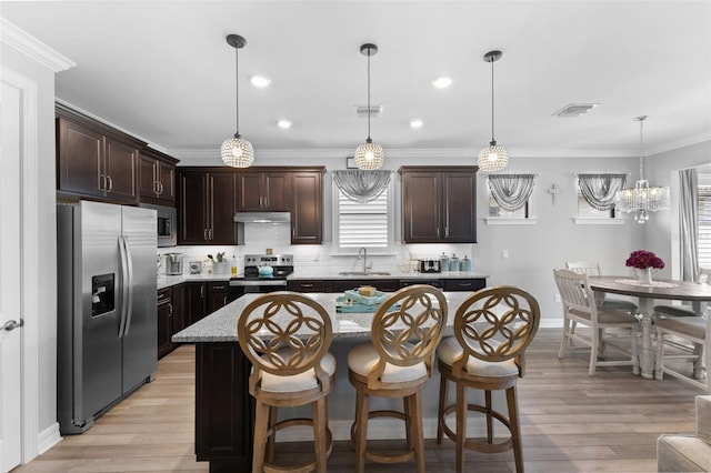 kitchen featuring decorative light fixtures, a kitchen island, appliances with stainless steel finishes, a kitchen breakfast bar, and dark brown cabinetry