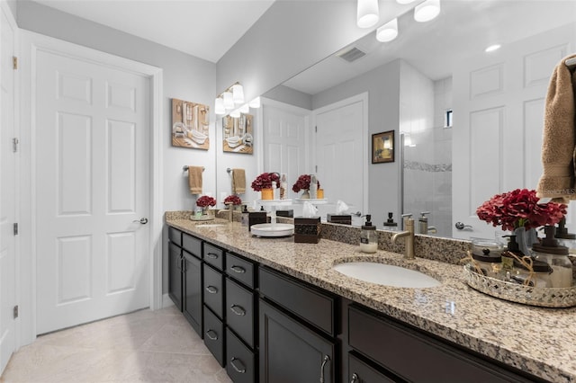 bathroom with tile patterned flooring, tiled shower, and vanity