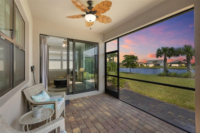 sunroom with ceiling fan and a water view