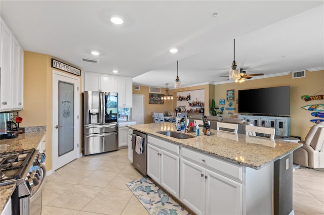 kitchen with appliances with stainless steel finishes, white cabinetry, sink, light tile patterned flooring, and a center island with sink