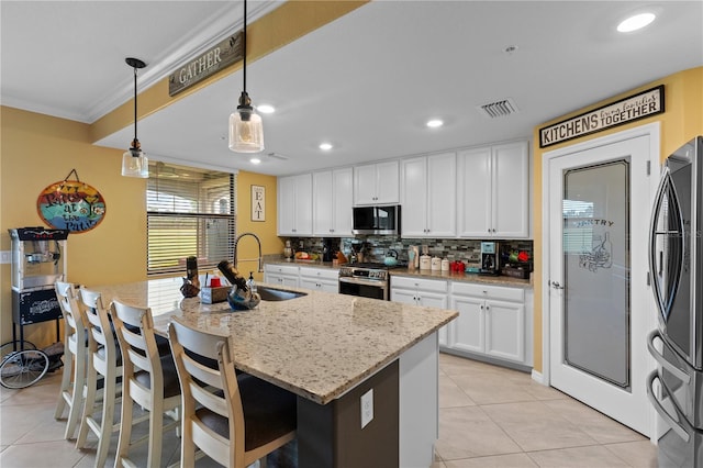 kitchen featuring a center island with sink, white cabinetry, hanging light fixtures, appliances with stainless steel finishes, and light stone counters