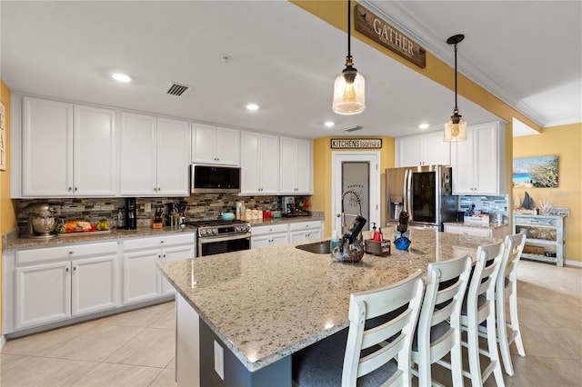 kitchen with hanging light fixtures, light stone countertops, appliances with stainless steel finishes, an island with sink, and white cabinets