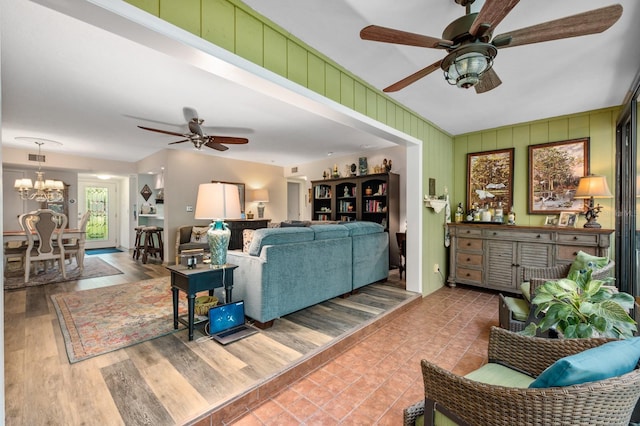 living room featuring ceiling fan with notable chandelier, wooden walls, and hardwood / wood-style flooring