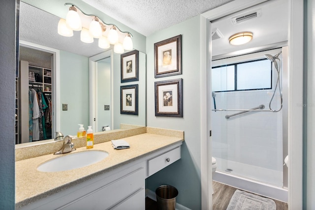 bathroom featuring toilet, a textured ceiling, a shower with shower door, wood-type flooring, and vanity