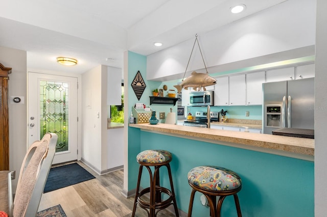 kitchen with hanging light fixtures, a kitchen bar, light wood-type flooring, white cabinetry, and appliances with stainless steel finishes