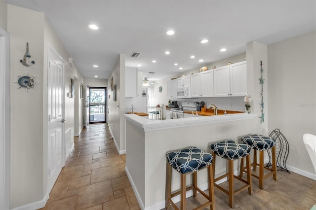 kitchen with ceiling fan, kitchen peninsula, white appliances, a breakfast bar area, and white cabinets