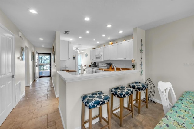 kitchen with kitchen peninsula, ceiling fan, white appliances, a kitchen breakfast bar, and white cabinets