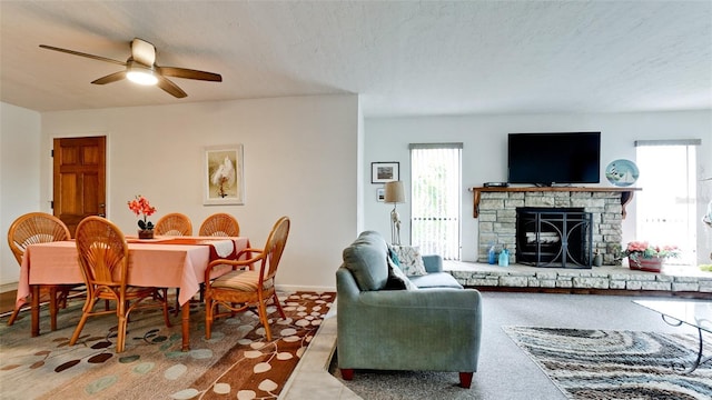 living room featuring a textured ceiling, ceiling fan, and a stone fireplace