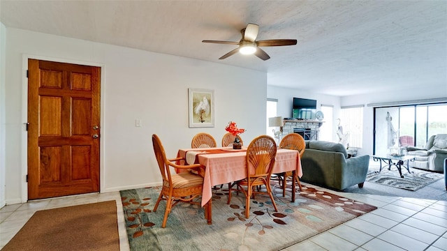 tiled dining space featuring a fireplace, ceiling fan, and a textured ceiling