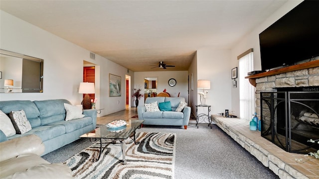 living room with a stone fireplace, ceiling fan, and carpet