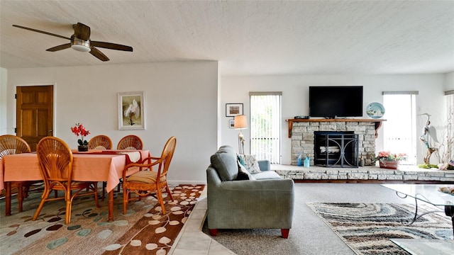 tiled living room featuring a textured ceiling, ceiling fan, and a stone fireplace