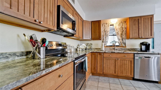 kitchen featuring dark stone countertops, stainless steel appliances, a textured ceiling, sink, and light tile patterned flooring