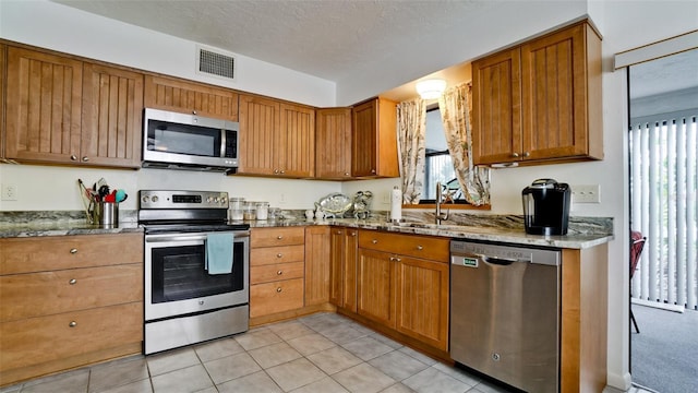 kitchen featuring a textured ceiling, a healthy amount of sunlight, stone counters, and appliances with stainless steel finishes