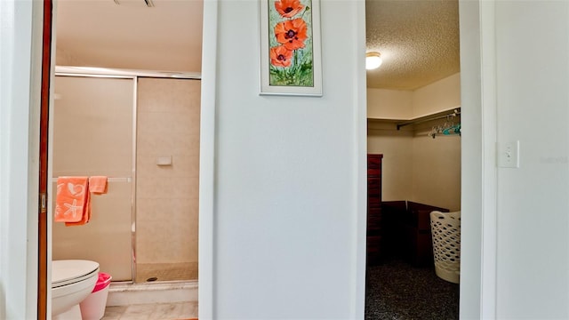 bathroom featuring toilet, an enclosed shower, and a textured ceiling