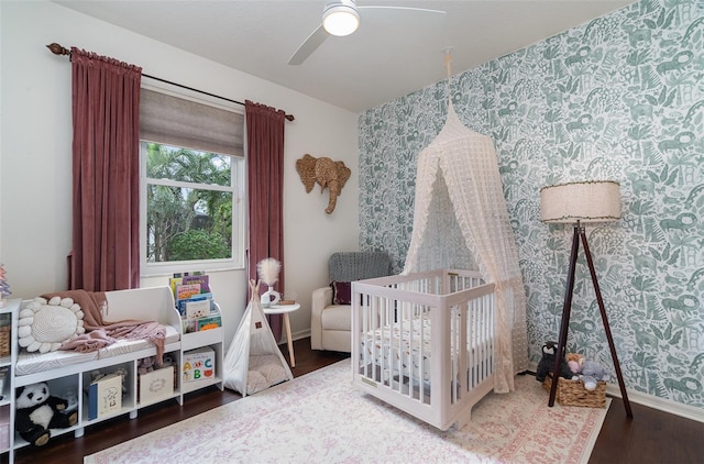 bedroom featuring ceiling fan, hardwood / wood-style floors, and a nursery area