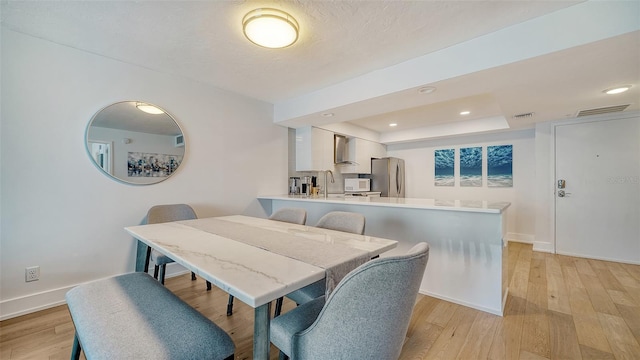 dining area with light wood-type flooring, a tray ceiling, and sink