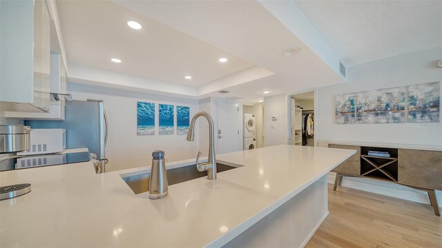 kitchen featuring light hardwood / wood-style flooring, stacked washer and dryer, range, white cabinets, and sink