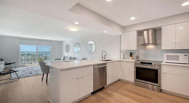 kitchen with white cabinets, stainless steel appliances, kitchen peninsula, wall chimney exhaust hood, and sink