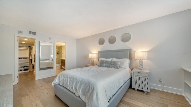 bedroom with a walk in closet, a closet, ensuite bathroom, and light hardwood / wood-style floors