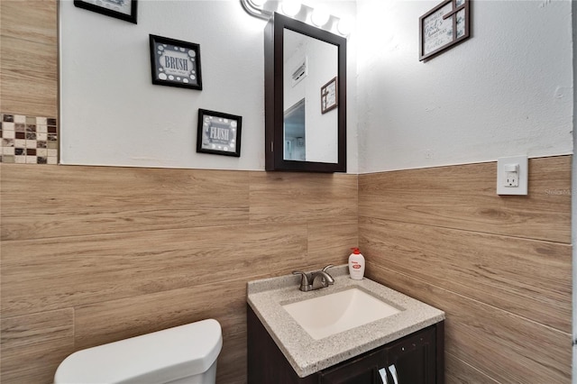 bathroom featuring vanity, tile walls, and toilet