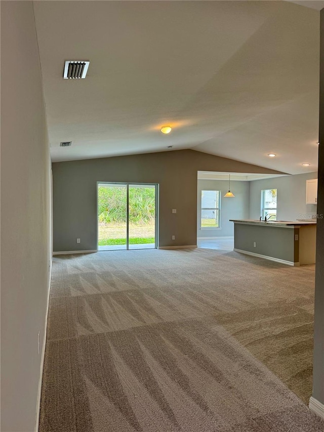 unfurnished living room featuring light carpet, lofted ceiling, and plenty of natural light