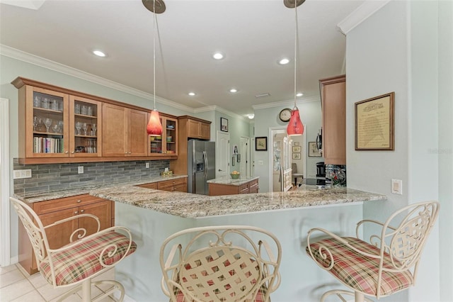 kitchen with light stone counters, kitchen peninsula, a breakfast bar area, stainless steel fridge with ice dispenser, and pendant lighting