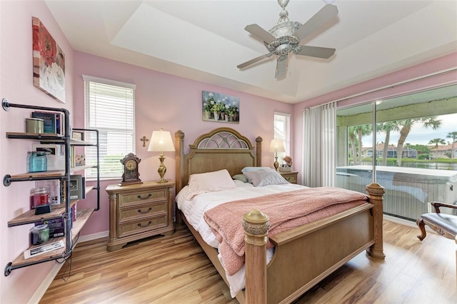 bedroom featuring ceiling fan, light hardwood / wood-style flooring, multiple windows, and a tray ceiling