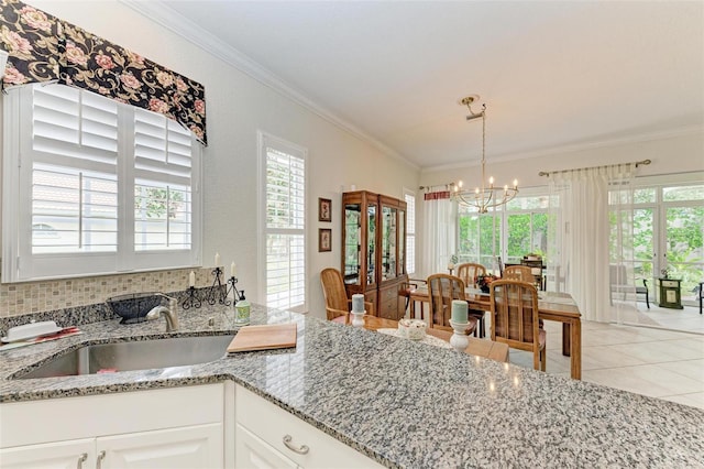 kitchen with sink, decorative light fixtures, white cabinetry, light stone countertops, and a notable chandelier