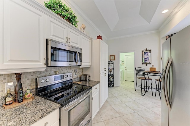 kitchen with stainless steel appliances, decorative backsplash, a tray ceiling, white cabinets, and dark stone countertops