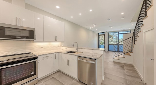 kitchen featuring a peninsula, a sink, white cabinets, appliances with stainless steel finishes, and light stone countertops