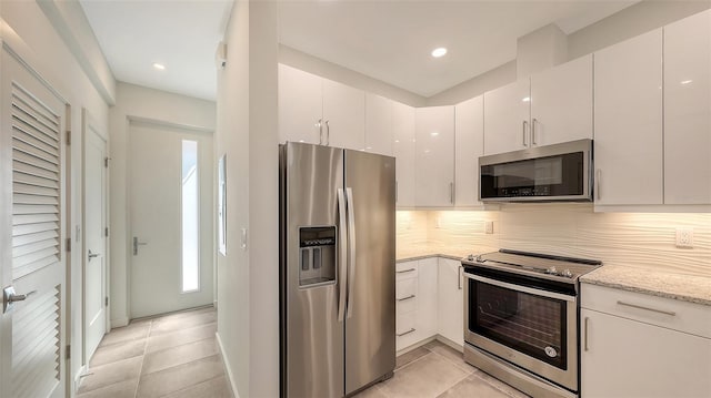 kitchen featuring light stone counters, tasteful backsplash, appliances with stainless steel finishes, light tile patterned flooring, and white cabinetry