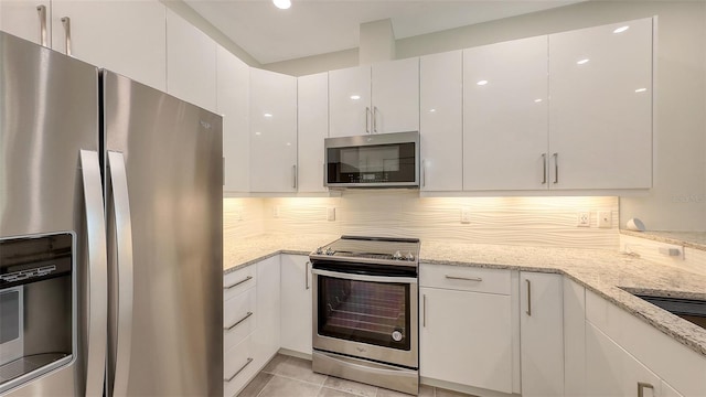 kitchen featuring stainless steel appliances, white cabinetry, backsplash, and light stone counters