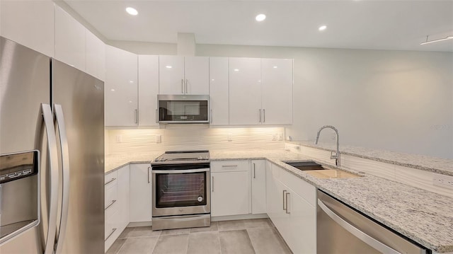 kitchen featuring light stone counters, stainless steel appliances, white cabinetry, a sink, and a peninsula