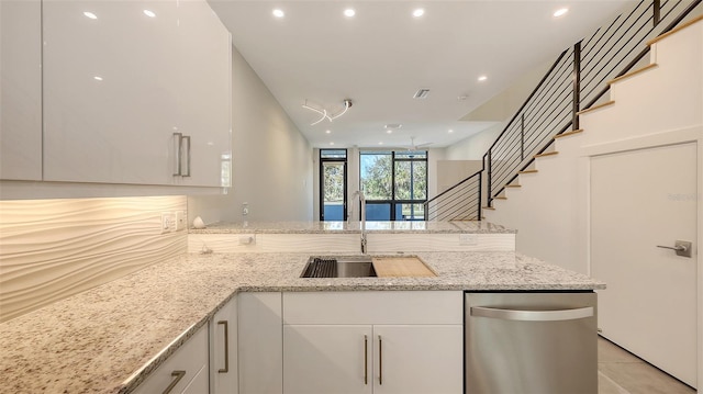 kitchen with white cabinets, dishwasher, light stone counters, a peninsula, and a sink