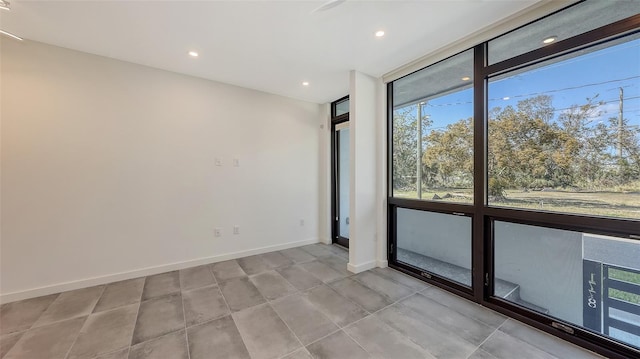 empty room with light tile patterned floors, a wall of windows, recessed lighting, and baseboards