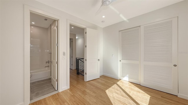 unfurnished bedroom featuring a closet, baseboards, light wood finished floors, and ensuite bathroom