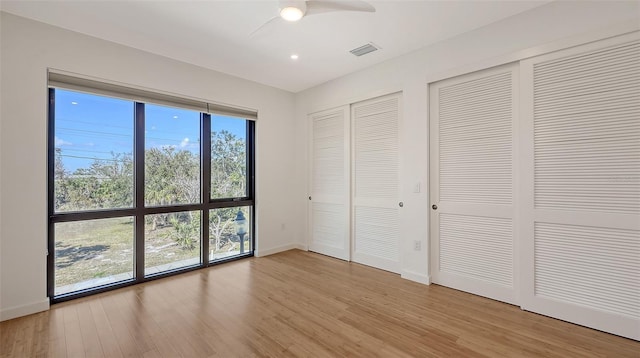 unfurnished bedroom featuring baseboards, visible vents, light wood finished floors, and two closets