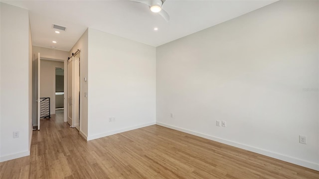 unfurnished room with a barn door, visible vents, baseboards, a ceiling fan, and light wood-style floors