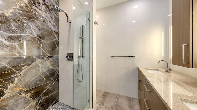 full bathroom featuring double vanity, a stall shower, tile walls, and a sink