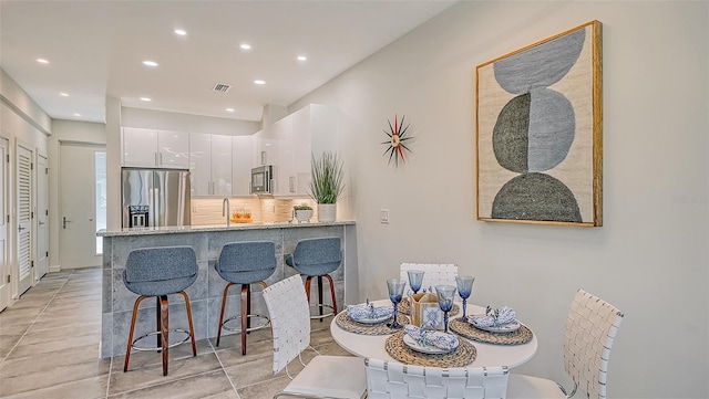 kitchen with kitchen peninsula, light stone countertops, stainless steel fridge with ice dispenser, a breakfast bar area, and white cabinets