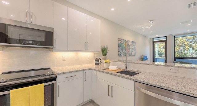 kitchen featuring light stone countertops, a sink, decorative backsplash, stainless steel appliances, and white cabinetry