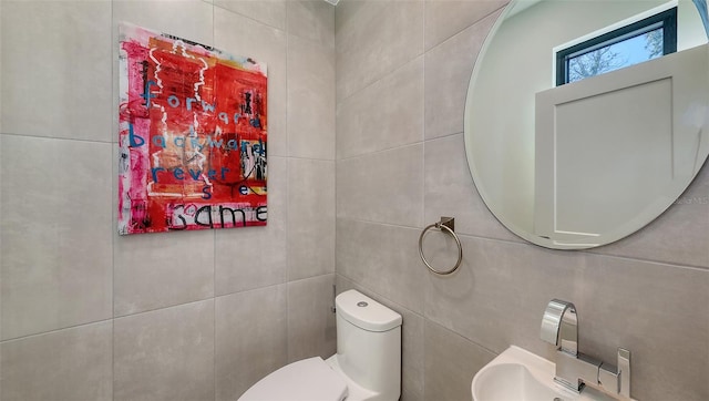 half bath featuring toilet, tile walls, and a sink