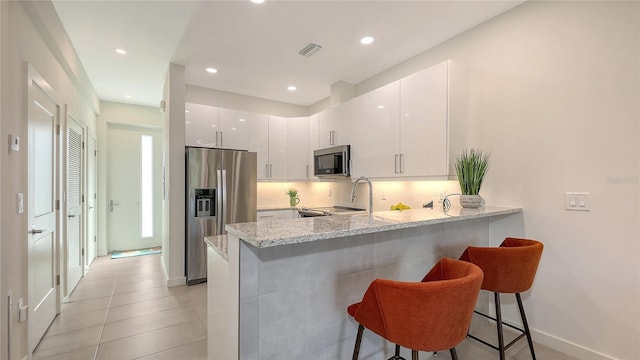 kitchen featuring a kitchen bar, visible vents, backsplash, stainless steel appliances, and a peninsula