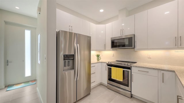 kitchen with tasteful backsplash, light stone countertops, light tile patterned floors, appliances with stainless steel finishes, and white cabinetry