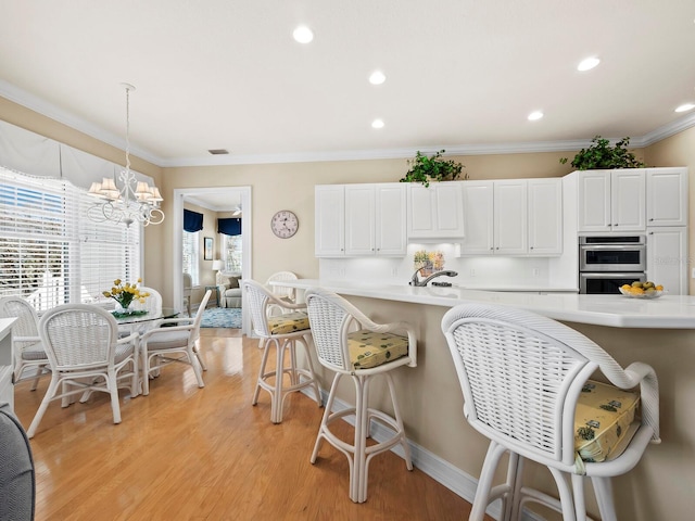 kitchen with double oven, ornamental molding, white cabinets, decorative light fixtures, and light wood-type flooring