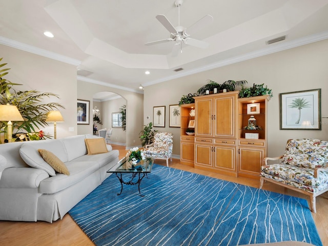 living room featuring hardwood / wood-style flooring, crown molding, ceiling fan, and a tray ceiling