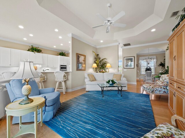 living room featuring a tray ceiling, ornamental molding, ceiling fan, and light wood-type flooring