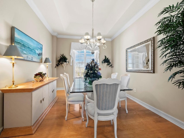 dining room featuring an inviting chandelier, crown molding, a raised ceiling, and light wood-type flooring