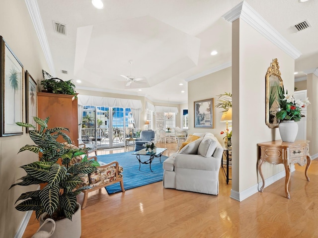 living room with crown molding, ceiling fan with notable chandelier, a raised ceiling, and light hardwood / wood-style floors